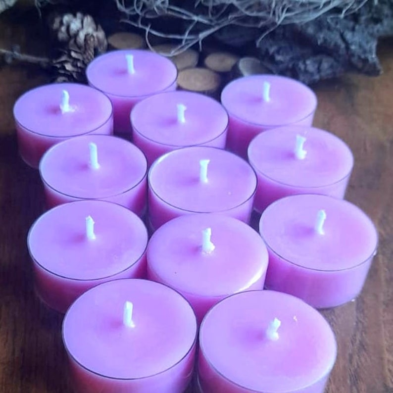 May include: A group of 10 lavender-colored tea light candles arranged in a circle on a wooden surface. The candles are unscented and have a white wick in the center.