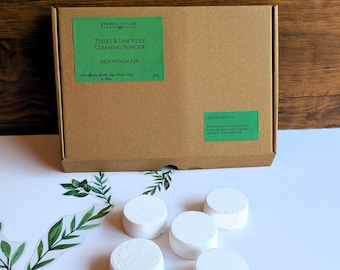 May include: A brown cardboard box labeled Starch House Toilet & Sink Fizzy Cleaning Powder in Mountain Air, 250g, with an ingredients list. Five round, white, solid cleaning tablets are arranged in front of the box on a white surface.