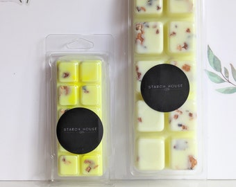 May include: Two clear plastic containers of wax melts. The wax melts are yellow with small brown flecks. The containers have black labels that say "Starch House Co."