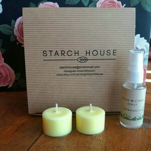 May include: A brown cardboard box with the text "STARCH HOUSE" printed on it. The box is next to two yellow tea light candles and a small bottle of room and linen spray labeled "Citronella".