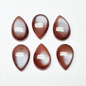 May include: Six teardrop-shaped gemstone cabochons with a brown and iridescent finish. The cabochons are arranged in two rows of three.