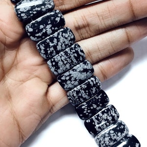 Könnte beinhalten: Eine Reihe schwarzer und weißer Schneeflocken-Obsidianperlen. Die Perlen sind rechteckig und haben ein gesprenkeltes Muster.