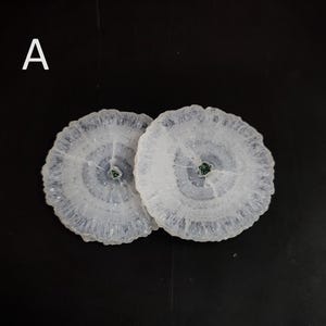 May include: Two white agate coasters with a blue and white pattern and a green center. The coasters are round and have a smooth surface.