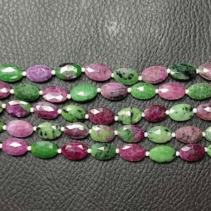 May include: A strand of oval-shaped green and pink gemstone beads. The beads are faceted and have a polished finish.