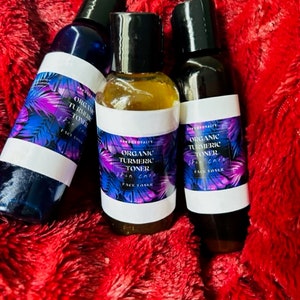 Puede incluir: Tres botellas de vidrio de tónico facial de cúrcuma orgánica. Las botellas están etiquetadas como "Tónico de cúrcuma orgánica Cuidado de la piel Tónico facial" y tienen un diseño morado y negro.