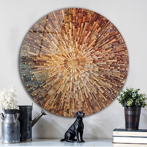 Puede incluir: Una gran obra de arte mural redonda con un diseño de explosión solar hecho de varias piezas de madera en tonos marrones, beige y naranja. La obra de arte está montada en una pared blanca sobre una cómoda blanca y azul. Una estatua de perro negro y plantas en macetas están en la cómoda.