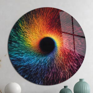 May include: A round wall art piece with a vibrant, swirling design. The artwork features a central black void surrounded by a spectrum of colors, including red, orange, yellow, green, and blue. The piece is displayed on a wall above a wooden table.