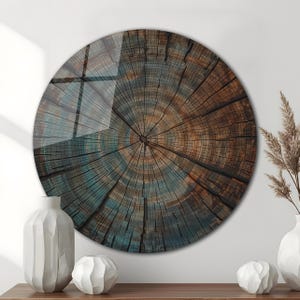 Könnte beinhalten: Runde Wandkunst mit einem Querschnitt eines Baumstamms. Das Kunstwerk zeigt konzentrische Ringe in Braun- und Türkistönen mit glänzendem Finish. Das Stück hängt an einer Wand, mit weißen Vasen und dekorativen Elementen im Vordergrund. Durchmesser: ca. 76 cm.