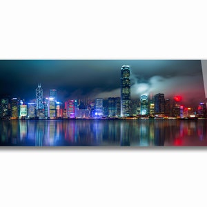 May include: A panoramic view of the Hong Kong skyline at night. The city is illuminated with colorful lights, reflecting in the water below. The skyscrapers are tall and slender, with a few taller buildings standing out. The sky is dark and cloudy, with a hint of fog.