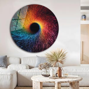May include: A large, round wall art piece featuring a vibrant, abstract design. The artwork showcases a central black vortex, surrounded by radiating lines of color, transitioning from blue to red and yellow. The piece is mounted on a white wall.
