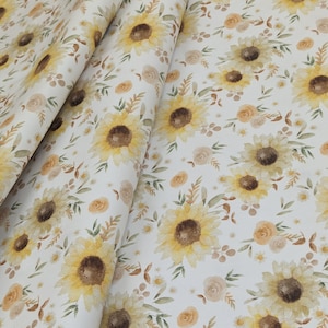 May include: White fabric with a repeating pattern of yellow sunflowers, green leaves, and small brown and orange flowers.