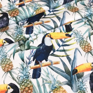 May include: White fabric with a tropical print featuring toucans and pineapples. The toucans are blue, black, and yellow with long orange beaks. The pineapples are green and yellow.