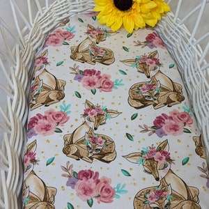 May include: White wicker basket with a white and gold fabric liner featuring a repeating pattern of brown deer with floral crowns and pink flowers. A yellow sunflower is on top of the basket.