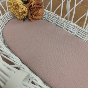 May include: A white wicker basket with a pink fitted sheet inside. The basket is empty and has a handle on the top. There are three yellow and orange silk flowers on top of the basket.