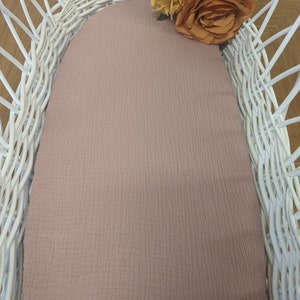 May include: A white wicker basket with a light pink fabric liner. The basket is decorated with a bouquet of yellow and orange flowers.