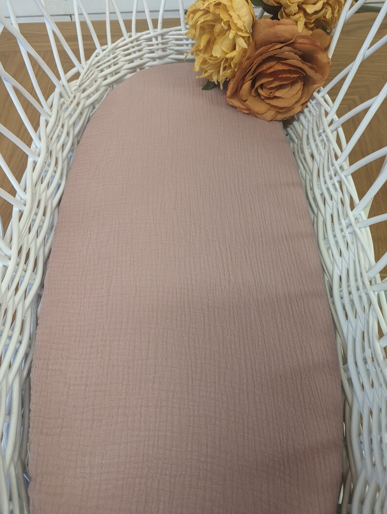 May include: A white wicker basket with a light pink fabric liner. The basket is decorated with a bouquet of yellow and orange flowers.