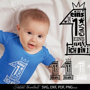 Schwarzes typografisches Design mit der Zahl 1 in kreativer Schriftgestaltung und kleinen Sternen sowie Herzsymbolen, kombiniert mit dem Text „Ich bin 1“ und mehrfach wiederholtem Wort „eins“. Das Motiv ist auf einem hellblauen Babybody dargestellt und zusätzlich in verschiedenen Farbvarianten als Grafik gezeigt. Perfekt geeignet für den ersten Geburtstag eines Kindes, für DIY Projekte wie Kleidung, Deko oder personalisierte Geschenke zur Feier des ersten Lebensjahres.