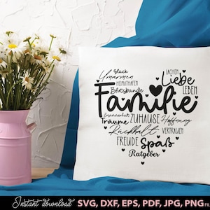 May include: A white cushion featuring the word "Familie" in a heart shape, with German words around it. A pink vase holding white daisies is on the left. The cushion rests on a blue surface.