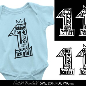 Schwarzes typografisches Design mit der Zahl 1 in kreativer Schriftgestaltung und kleinen Sternen sowie Herzsymbolen, kombiniert mit dem Text „Ich bin 1“ und mehrfach wiederholtem Wort „eins“. Das Motiv ist auf einem hellblauen Babybody dargestellt und zusätzlich in verschiedenen Farbvarianten als Grafik gezeigt. Perfekt geeignet für den ersten Geburtstag eines Kindes, für DIY Projekte wie Kleidung, Deko oder personalisierte Geschenke zur Feier des ersten Lebensjahres.