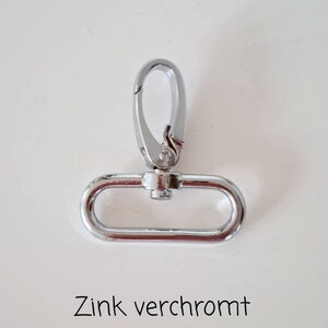 May include: A silver-toned metal clasp with a hook and a D-ring. The text "Zink verchromt" is written below the clasp.