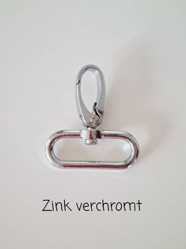 May include: A silver-toned metal clasp with a hook and a D-ring. The text "Zink verchromt" is written below the clasp.