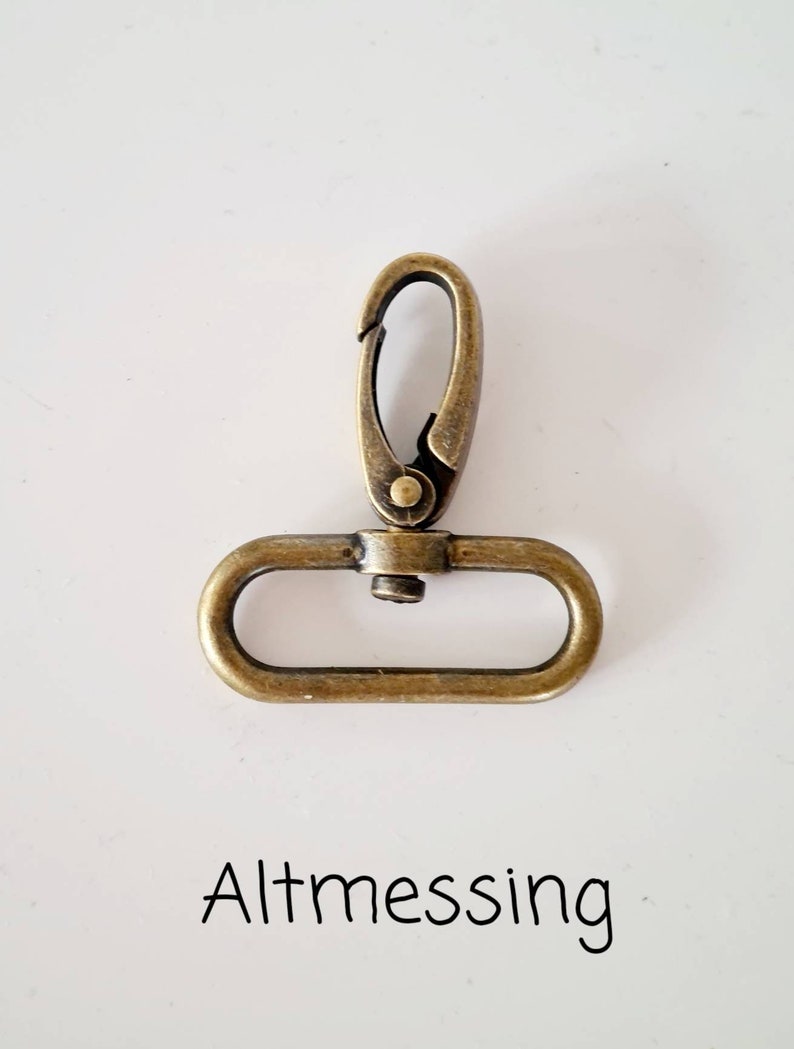 May include: A gold-toned metal clasp with a spring-loaded opening. The clasp is designed for attaching to a strap or chain.