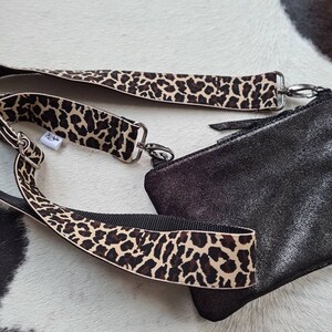 May include: A black leather crossbody bag with a leopard print strap. The bag has a zip closure and a silver chain detail.