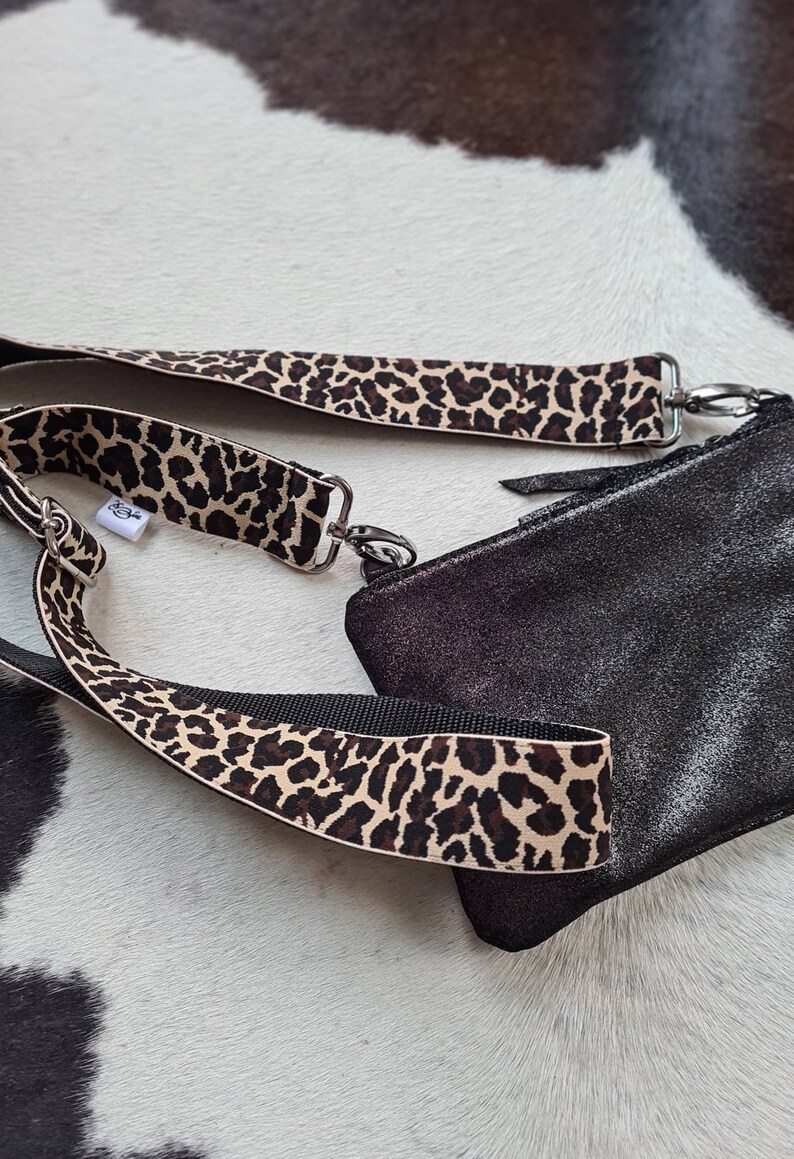 May include: A black leather crossbody bag with a leopard print strap. The bag has a zip closure and a silver chain detail.