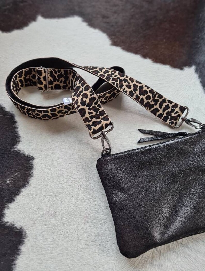 May include: A black leather purse with a leopard print adjustable strap. The strap is made of a black and brown fabric with a leopard print pattern.