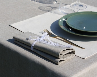 May include: A folded linen napkin tied with a white lace ribbon, a gold fork, and two green ceramic plates on a white placemat on a gray linen tablecloth.