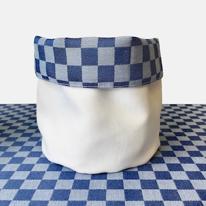 May include: A white fabric storage basket with a blue and white checkered trim. The basket is sitting on a blue and white checkered surface.