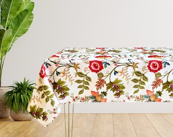 Puede incluir: Mantel blanco con un patrón floral con flores y hojas rojas, rosas y verdes. El mantel está drapeado sobre una mesa con patas de metal dorado.