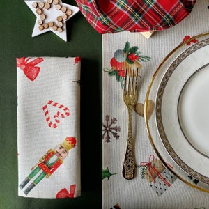May include: A white linen napkin with a red and white candy cane, a nutcracker, and a red bow. The napkin is folded and placed on a green surface.