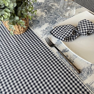 May include: A black and white checkered tablecloth with a white tablecloth with a blue and white floral pattern on top. A white plate with a black and white checkered napkin folded into a bow is on top of the white tablecloth. A silver fork is on the white tablecloth.