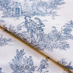 Puede incluir: Una tela doblada con un diseño toile de Jouy azul y blanco. El patrón representa una escena pastoril con figuras, un pequeño edificio y follaje. La tela está doblada, mostrando la impresión detallada y el fondo blanquecino.