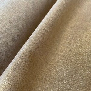 Peut inclure: Gros plan sur un tissu beige avec un léger chatoiement. Le tissu a une texture tissée et un léger reflet iridescent.