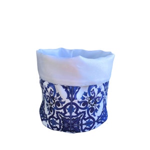 Puede incluir: Una cesta de almacenamiento de tela blanca con un diseño estampado azul y blanco. El patrón presenta intrincados motivos florales y geométricos.