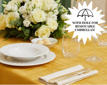 Puede incluir: Una mesa de comedor formal con un mantel amarillo, platos blancos, cubiertos dorados y vasos transparentes con bordes dorados. Un arreglo floral de rosas blancas y vegetación se encuentra en el fondo. El texto dice "WITH HOLE FOR REMOVABLE UMBRELLAS!"