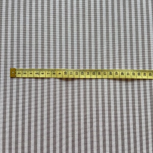 Puede incluir: Primer plano de una tela a rayas blancas y grises con una cinta m&eacute;trica colocada sobre ella. La cinta mide 63,5 cm.