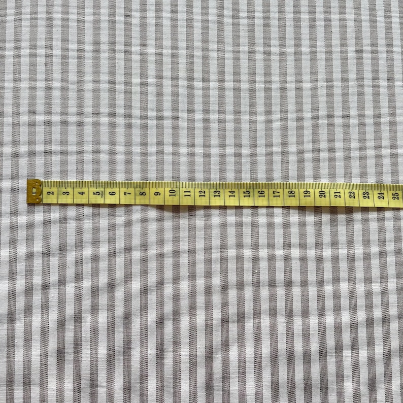 Puede incluir: Primer plano de una tela a rayas blancas y grises con una cinta m&eacute;trica colocada sobre ella. La cinta mide 63,5 cm.