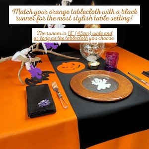 Puede incluir: Una mesa puesta para Halloween con un mantel naranja y un camino de mesa negro. El camino de mesa tiene 45 cm de ancho. La mesa está decorada con un mantel individual con forma de calabaza, un plato con forma de fantasma y una servilleta negra con un diseño de telaraña.
