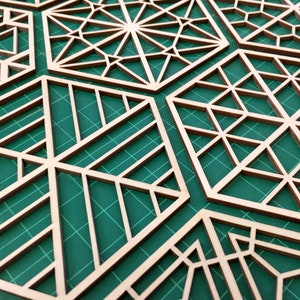 May include: A set of eight wooden geometric shapes with intricate cut-out designs. The shapes are arranged on a green cutting mat.
