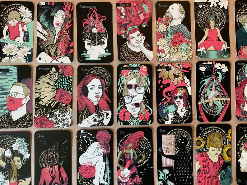 Pu&ograve; includere: Un set di 22 carte dei tarocchi con illustrazioni colorate che raffigurano persone e simboli. Le carte hanno uno sfondo nero con accenti dorati. I nomi delle carte sono stampati in lettere dorate nella parte superiore di ogni carta. Le carte sono disposte in tre file di sette carte.