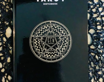 Può includere: Libro nero con il titolo "Tarot Sketchbook" e un design a stella dorata con le parole "Next Gen Tarot" all'interno. Il libro ha anche il testo "Next Gen Tarot by Zsuzsa" in basso.