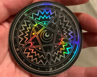 Può includere: Un adesivo nero e argento iridescente con un design a pentagramma e lune crescenti. L'adesivo ha una forma circolare e una finitura olografica.