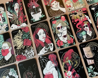 Op de afbeelding: Een set tarotkaarten met zwarte achtergronden en kleurrijke illustraties. De kaarten tonen verschillende personages en symbolen, waaronder een kat, een vrouw met een koptelefoon, een vrouw met een megafoon en een vrouw die gitaar speelt. De kaarten zijn genummerd en hebben de namen van de tarotsuits erop.