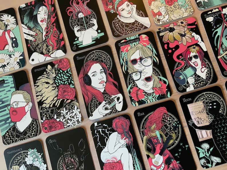 Pu&ograve; includere: Un set di carte dei tarocchi con sfondi neri e illustrazioni colorate. Le carte presentano vari personaggi e simboli, tra cui un gatto, una donna con le cuffie, una donna con un megafono e una donna che suona la chitarra. Le carte sono numerate e hanno i nomi dei semi dei tarocchi scritti su di esse.