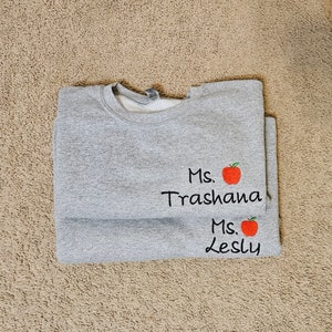 May include: Grey sweatshirt with the text "Ms. Trashana" and a red apple graphic, and the text "Ms. Lesly" and a red apple graphic.