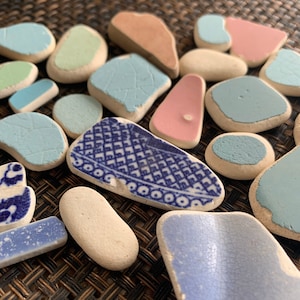 May include: A collection of blue and white ceramic tiles with a variety of patterns and designs. The tiles are arranged in a random pattern on a woven surface.