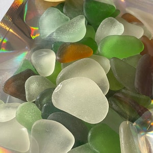 May include: A bag of sea glass in various shades of green, white, and brown. The sea glass is in the shape of hearts.
